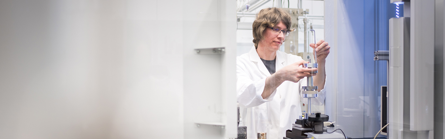 Mann hält Laboreinrichtung (metallischen Zylindrischen Kolben) in der Hand.