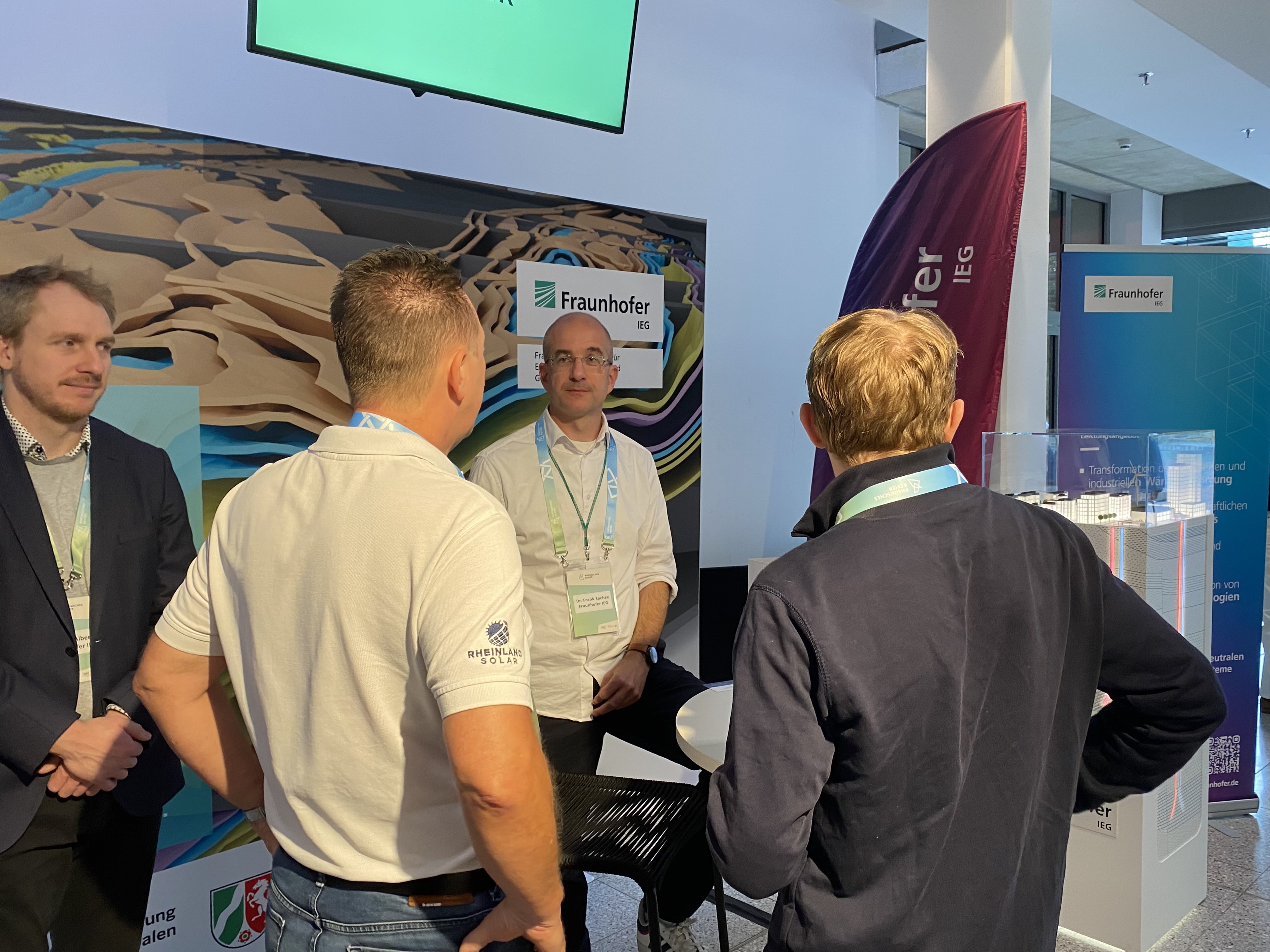 Im Foto sehen Sie Projektleiter Martin Albers (links) und Dr. Frank Sachse (rechts) am Messestand im Gespräch mit Besuchern. 